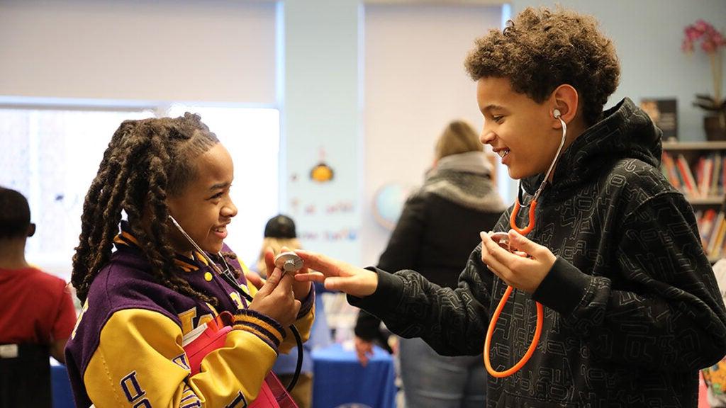 Students wear stethoscopes and practice using them together in a classroom